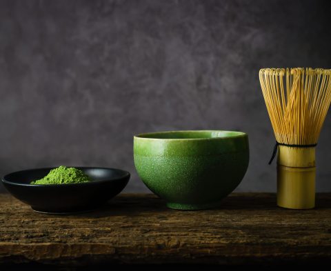 Japanese matcha green tea and matcha green tea powder at homemade clay bowl with bamboo whisk on wooden table with vignette tone